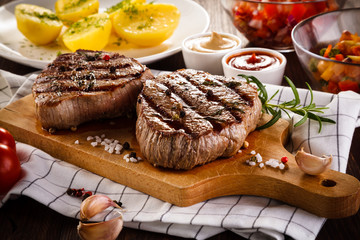 Grilled beefsteaks on cutting board on wooden table - dinner preparation