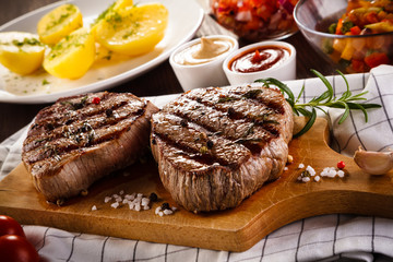 Grilled beefsteaks on cutting board on wooden table - dinner preparation