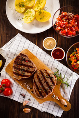 Grilled beefsteaks on cutting board on wooden table - dinner preparation