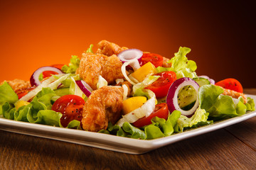 Salad with fried chicken strips on wooden table