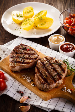 Grilled beefsteaks on cutting board on wooden table - dinner preparation