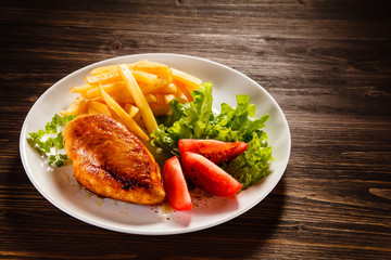 Grilled chicken fillet with french fries on wooden table