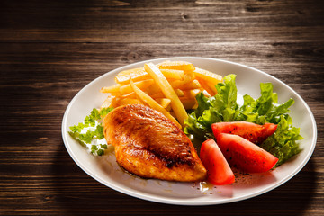 Grilled chicken fillet with french fries on wooden table