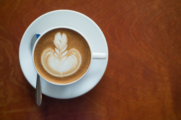 Cup of coffee with beautiful latte art on wooden table in coffee shop.