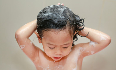 Little girl bathing and washing hair in bubble bath.