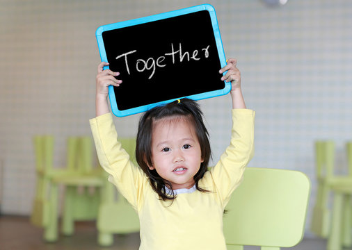Cute little child girl holding blackboard showing text " Together " in kids room. Education concept.