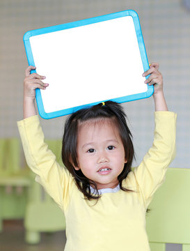 Cute asian child girl holding empty white blackboard in kids room.