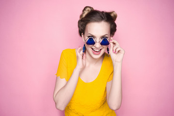 close-up portrait of a beautiful young blonde girl in fashionable sunglasses on a pink background in the studio in a yellow blouse and jeans holding a popular phone smiling