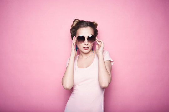 close-up portrait of young beautiful slim sexy young blonde woman in a retro pin-up style on pink background in studio wearing sunglasses smiling and posing