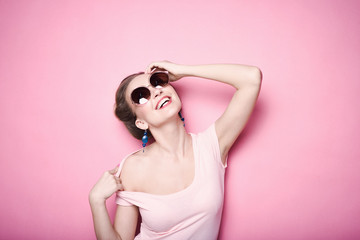 close-up portrait of young beautiful slim sexy young blonde woman in a retro pin-up style on pink background in studio wearing sunglasses smiling and posing