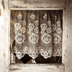 Close up of old house door window frame with broken glass and with white flower curtain