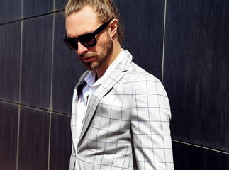 portrait of sexy handsome fashion male model man dressed in elegant white checkered suit .posing near dark blue wall in the street background in sunglasses