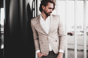 portrait of sexy handsome fashion male model man dressed in elegant beige checkered suit .posing on the street background