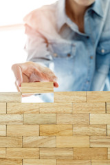 Hand of engineer playing a blocks wood tower game (jenga) on blueprint or architectural project concept.