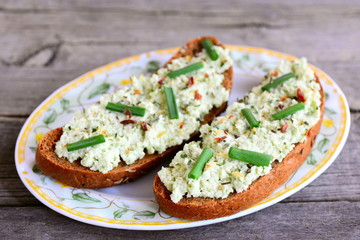 Guacamole toast on a plate and a vintage wooden background. Open rye sandwiches with guacamole, fresh green onion and spices. Homemade vegan toast recipe. Closeup