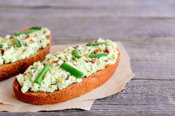 Rye bread toast with guacamole, fresh green onion and dried herbs on a paper and old wooden table. Veggie food idea for a picnic, breakfast or lunch. Healthy toast recipe