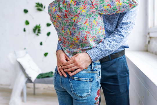 Closeup of couple at the white room. Man in a formal wear hugging by the waist a woman, wearing sexy jeans