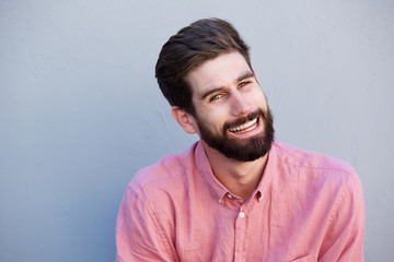 handsome man with beard laughing against gray wall