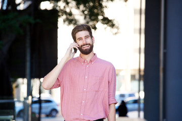 cheerful man walking on sidewalk and talking on smart phone