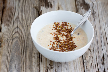 Fresh cooked oatmeal porridge with crushed linseed. On wooden table. Natural light, selective focus. 