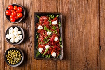 Beef carpaccio served with balls of mozzarella cheese, arugula and capers.