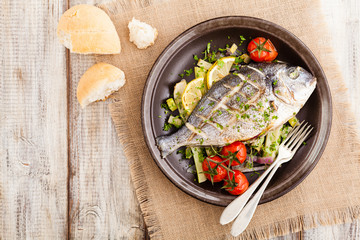 Baked whole fish, served with roasted vegetables and lemon.