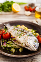 Baked whole fish, served with roasted vegetables and lemon.