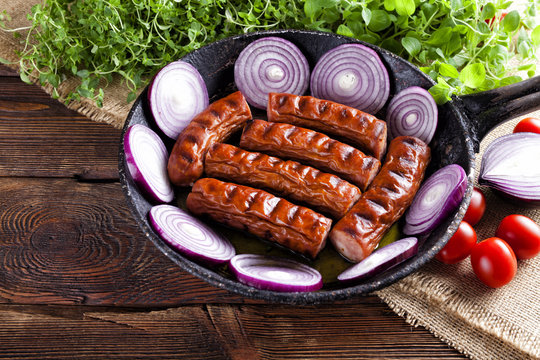Grilled sausage in a pan and fresh vegetables on wooden table