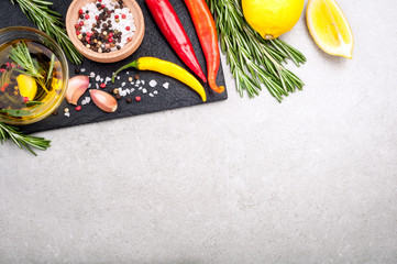 Herbs and spices background. Rosemary, lemon, olive oil, chili, salt and pepper on dark slate board top view. Copy space for your recipe