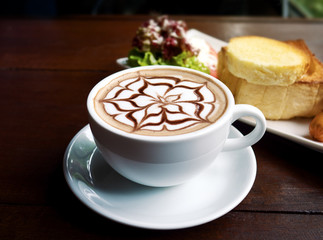 Coffee cup of latte art and breakfast set on wooden table in cafe.