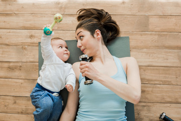 Top view of mother with baby boy lying on floor and playing with dumbbells