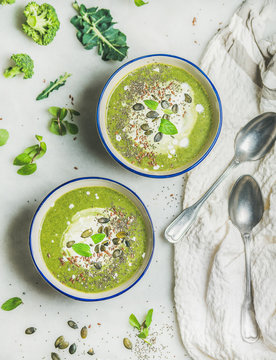 Spring detox broccoli green cream soup with mint and coconut cream in bowls over light marble background, top view. Clean eating, dieting, vegan, vegetarian, healthy food concept