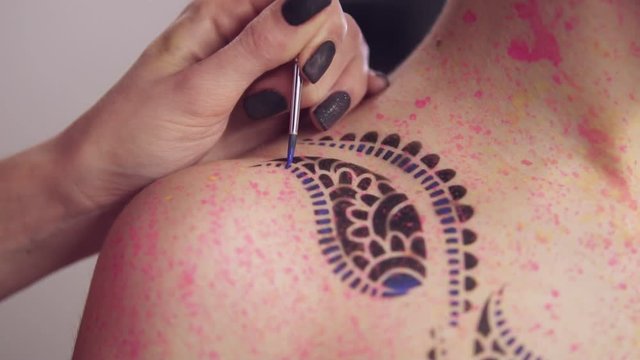 Master painting pattern on the girl's body using brush and different colors. Slowmotion shot