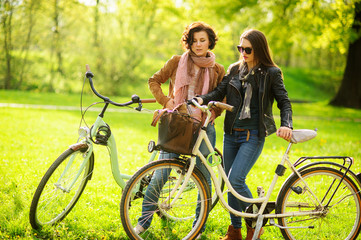 Two young attractive women ride bikes in the spring park.