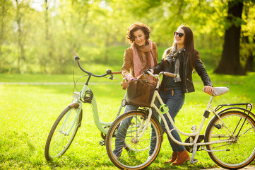 Plakat Two young attractive women ride bikes in the spring park.