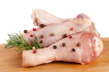 raw chicken drumsticks on a wooden cutting boardn with a sprig of dill and peppercorns white...