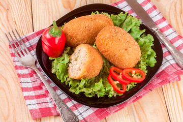 three fried breaded cutlet with lettuce on a black plate and wooden background