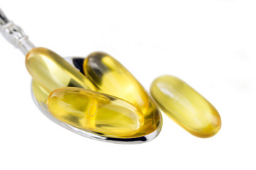 Yellow capsules omega 3, fatty acid, fish oil in the spoon isolated on white background