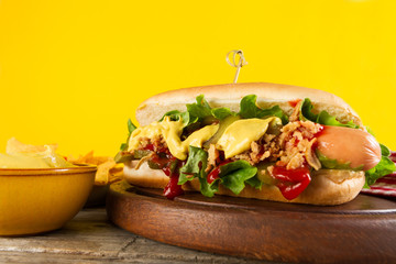 Tasty classic traditional hot dog on wooden board on yellow background.