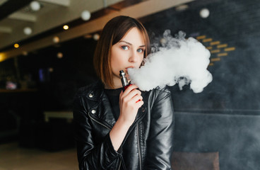 Vaping. Young beautiful girl smoking ( vaping ) e-cigarette with smoke outdoors. Vapor concept.