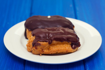 chocolated eclairs on white dish on wooden background