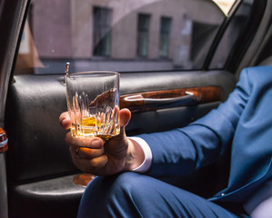 Human hand in the limousine holding glass of wiskey. Front closeup view