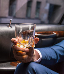 Human hand in the limousine holding glass of wiskey. Front closeup view