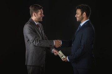 businessman giving money and bribing business partner isolated on black, businesspeople shaking hands concept