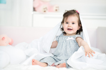 Fototapeta premium Sweet baby girl playing with a bed sheet in the bed. Shallow doff