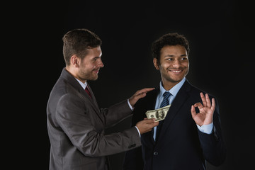 Businessman giving money and bribing business partner isolated on black