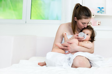 Mom and baby hugging in the bed, baby drinking a milk from the baby bottle. Shallow doff, copy space