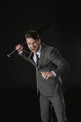 Angry businessman holding baseball bat and screaming isolated on black