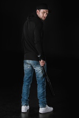 young robber in zoodie and cap with baseball bat isolated on black