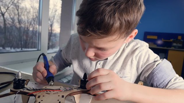 School boy soldering drone parts in the classroom. 4K.